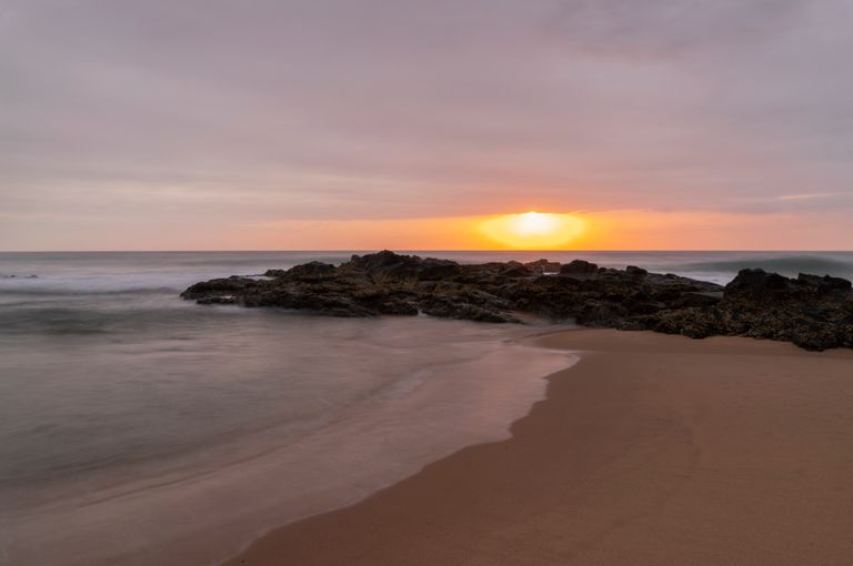 Peaceful sunrise at the Dolphin Coast with waves softly hitting the sandy shore and rocky formations.